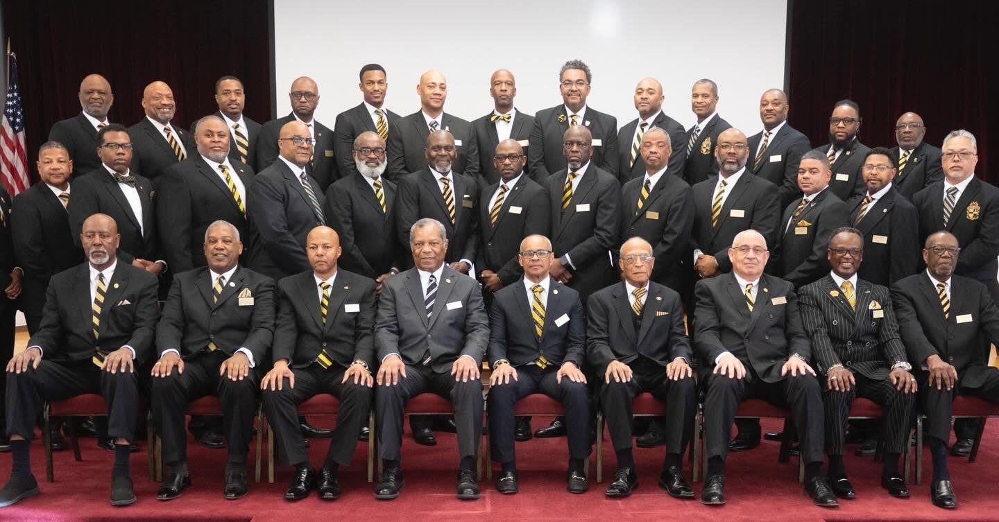 Brothers of Nu Omicron Lambda in dark suits and black-and-gold ties, seated and standing in three rows for a chapter portrait